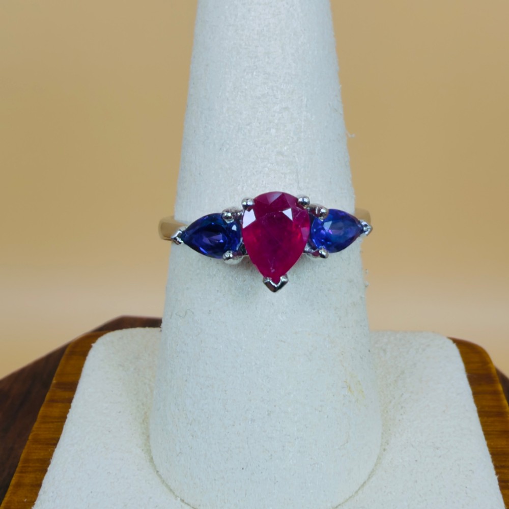 A platinum three-stone ring featuring a central pear-cut red ruby flanked by two pear-cut purple amethysts. View VI