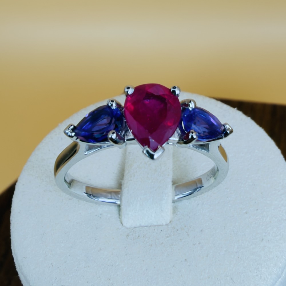 A platinum three-stone ring featuring a central pear-cut red ruby flanked by two pear-cut purple amethysts.