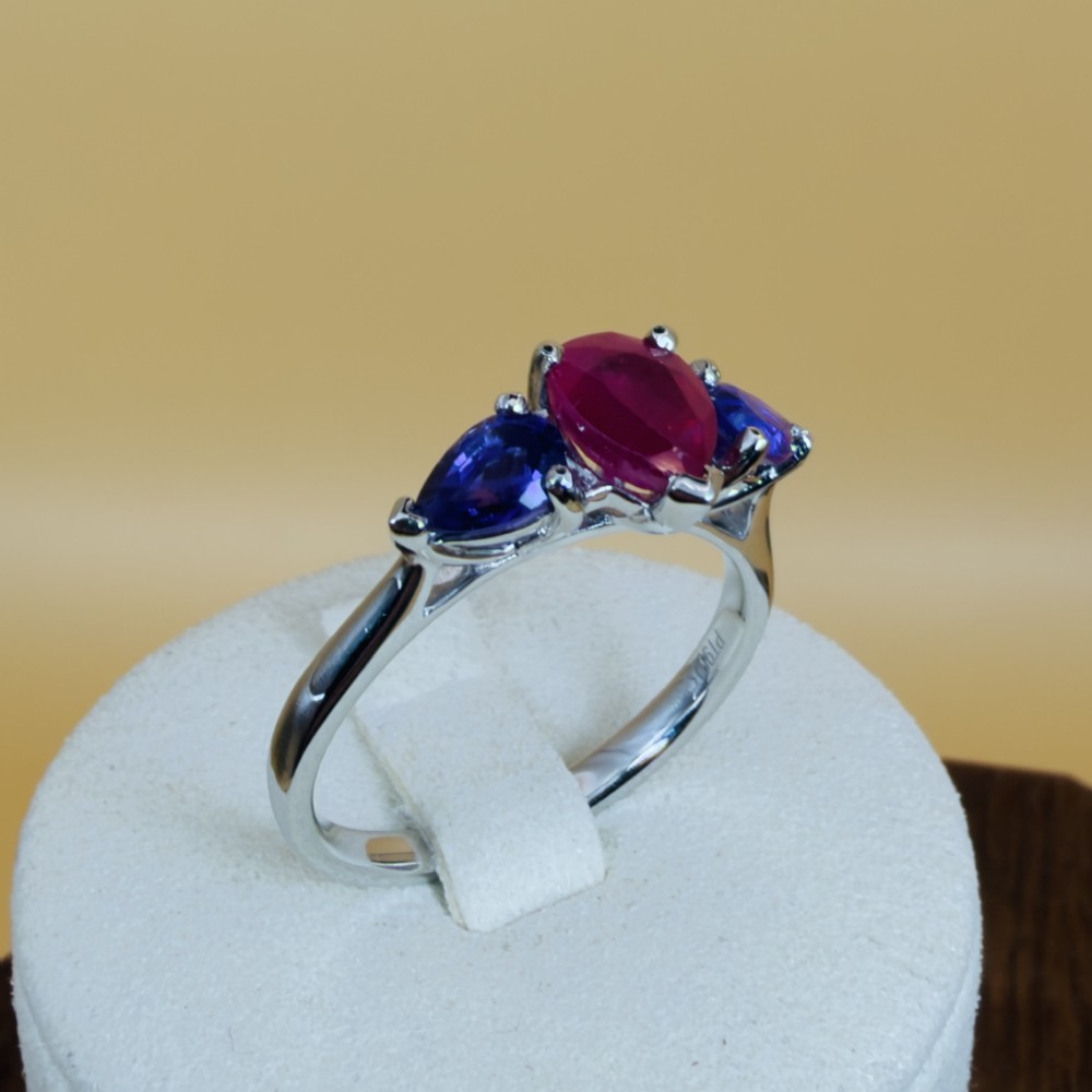 A platinum three-stone ring featuring a central pear-cut red ruby flanked by two pear-cut purple amethysts. View X