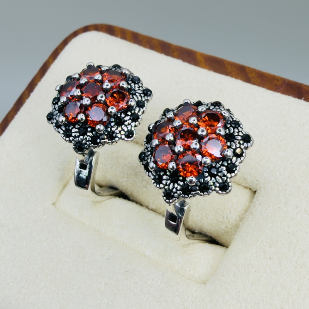 A pair of sterling silver hinge back cluster earrings featuring round faceted orange mandarin garnets encircled by small black tourmaline stones.