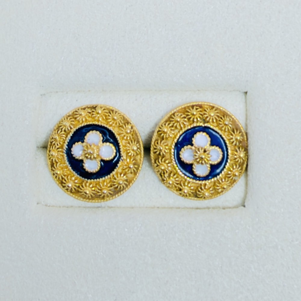 A pair of circular 19.2ct yellow gold stud earrings featuring a central white four-petalled flower against a dark blue enamel ground, surrounded by textured gold detail.