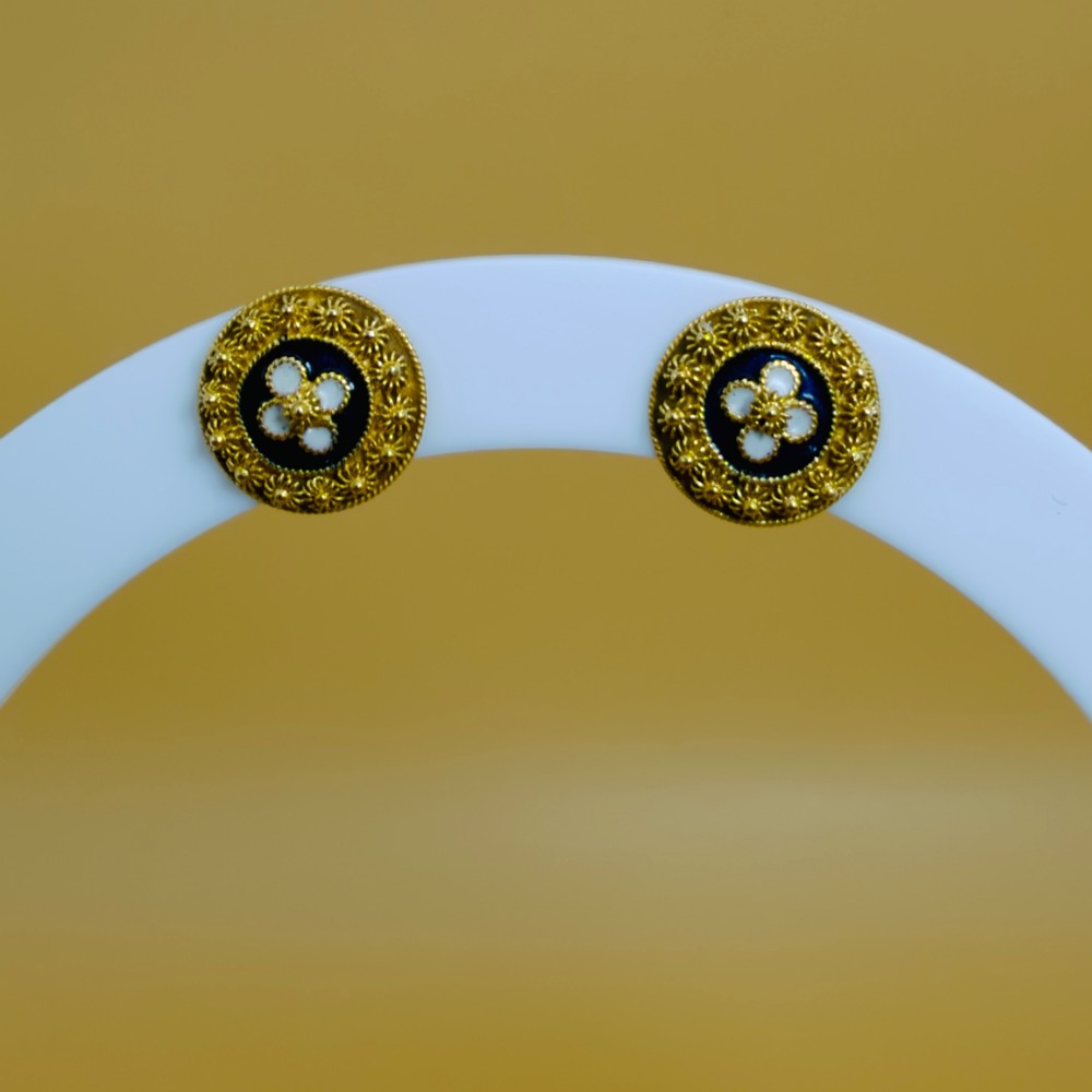 A pair of circular 19.2ct yellow gold stud earrings featuring a central white four-petalled flower against a dark blue enamel ground, surrounded by textured gold detail. View V