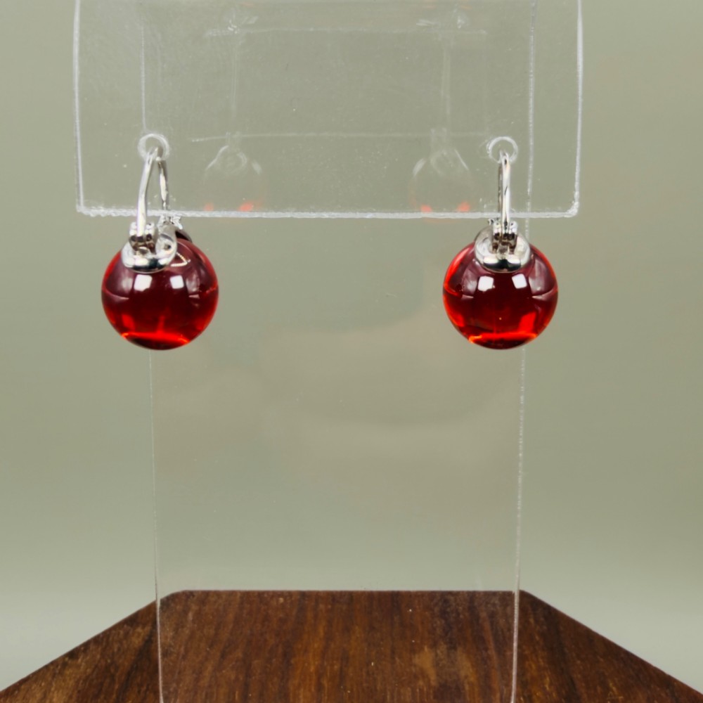 A pair of sterling silver drop earrings featuring translucent spherical red synthetic ruby beads suspended from hinge back hooks.