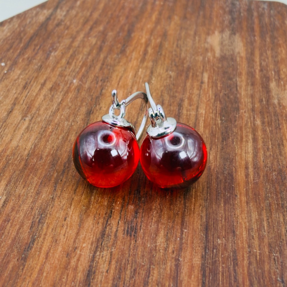 A pair of sterling silver drop earrings featuring translucent spherical red synthetic ruby beads suspended from hinge back hooks. View IV