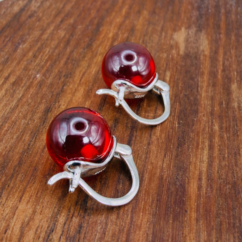 A pair of sterling silver drop earrings featuring translucent spherical red synthetic ruby beads suspended from hinge back hooks. View V