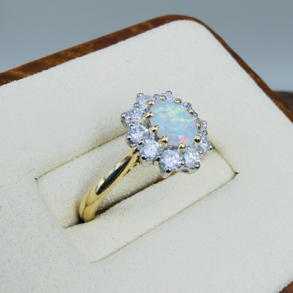 An 18ct yellow gold ring featuring an oval cabochon opal surrounded by a halo of brilliant-cut diamonds. View IV
