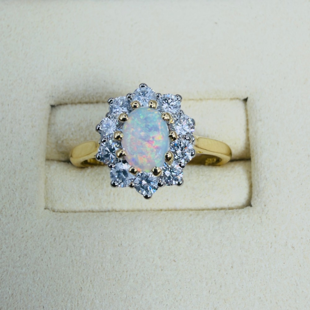 An 18ct yellow gold ring featuring an oval cabochon opal surrounded by a halo of brilliant-cut diamonds. View V