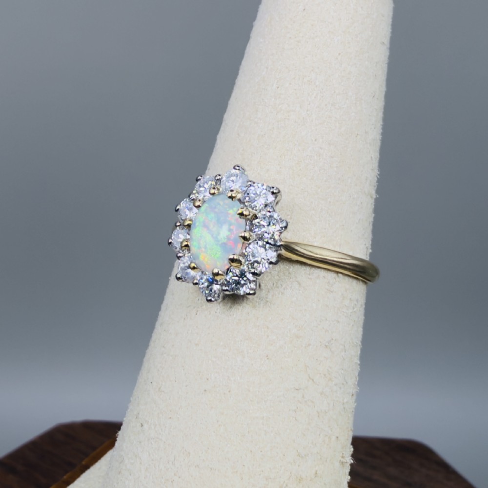 An 18ct yellow gold ring featuring an oval cabochon opal surrounded by a halo of brilliant-cut diamonds. View VII