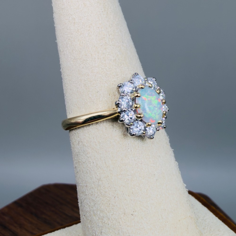 An 18ct yellow gold ring featuring an oval cabochon opal surrounded by a halo of brilliant-cut diamonds. View VIII