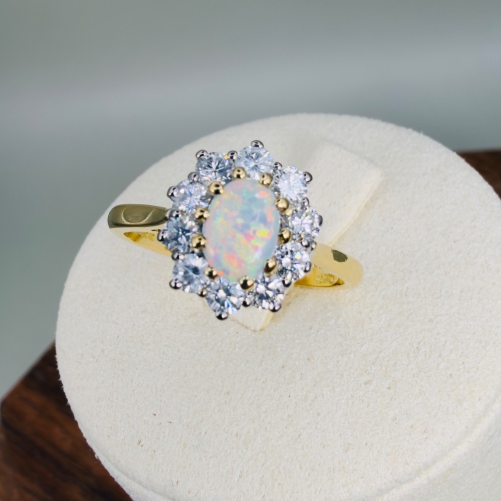 An 18ct yellow gold ring featuring an oval cabochon opal surrounded by a halo of brilliant-cut diamonds.