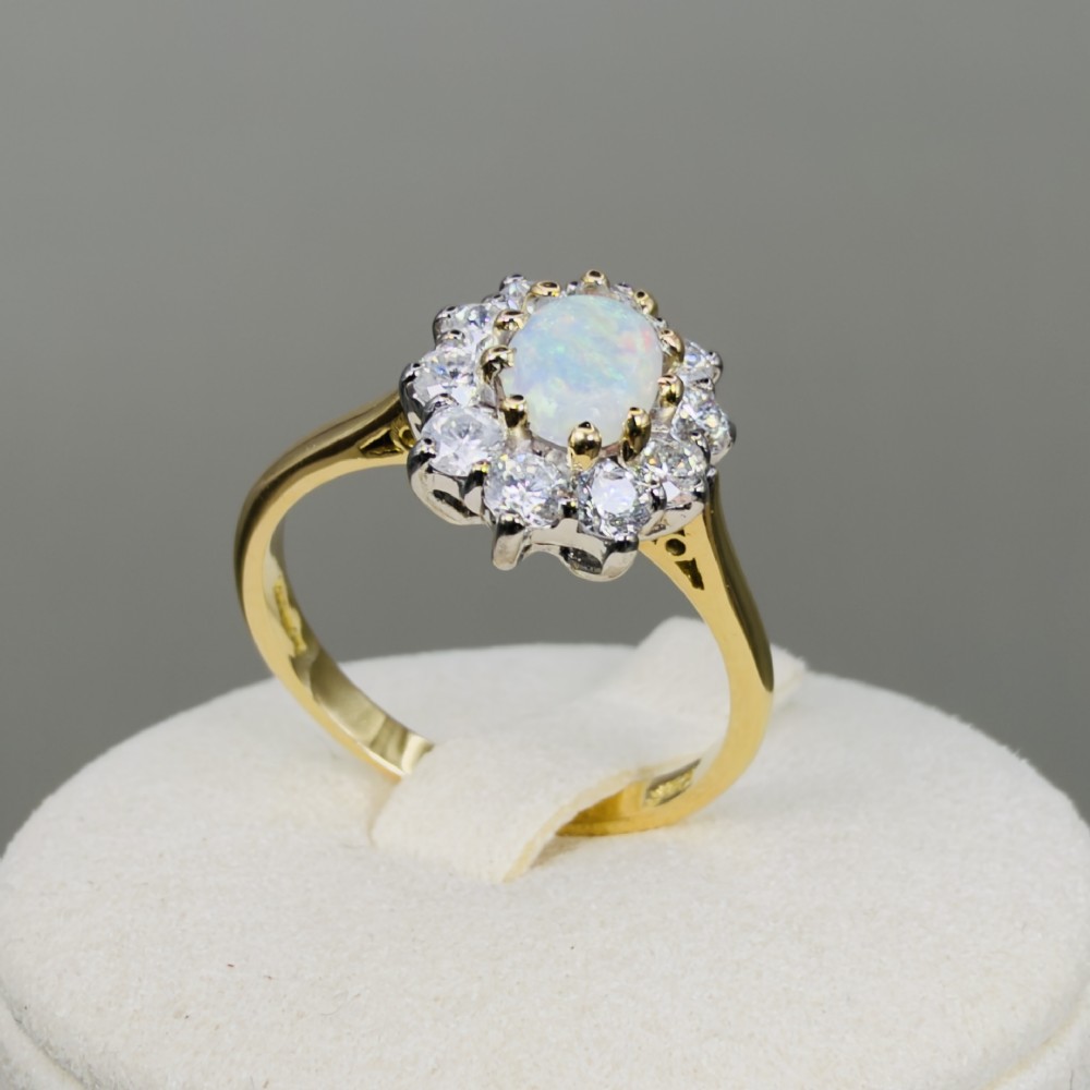 An 18ct yellow gold ring featuring an oval cabochon opal surrounded by a halo of brilliant-cut diamonds. View IX