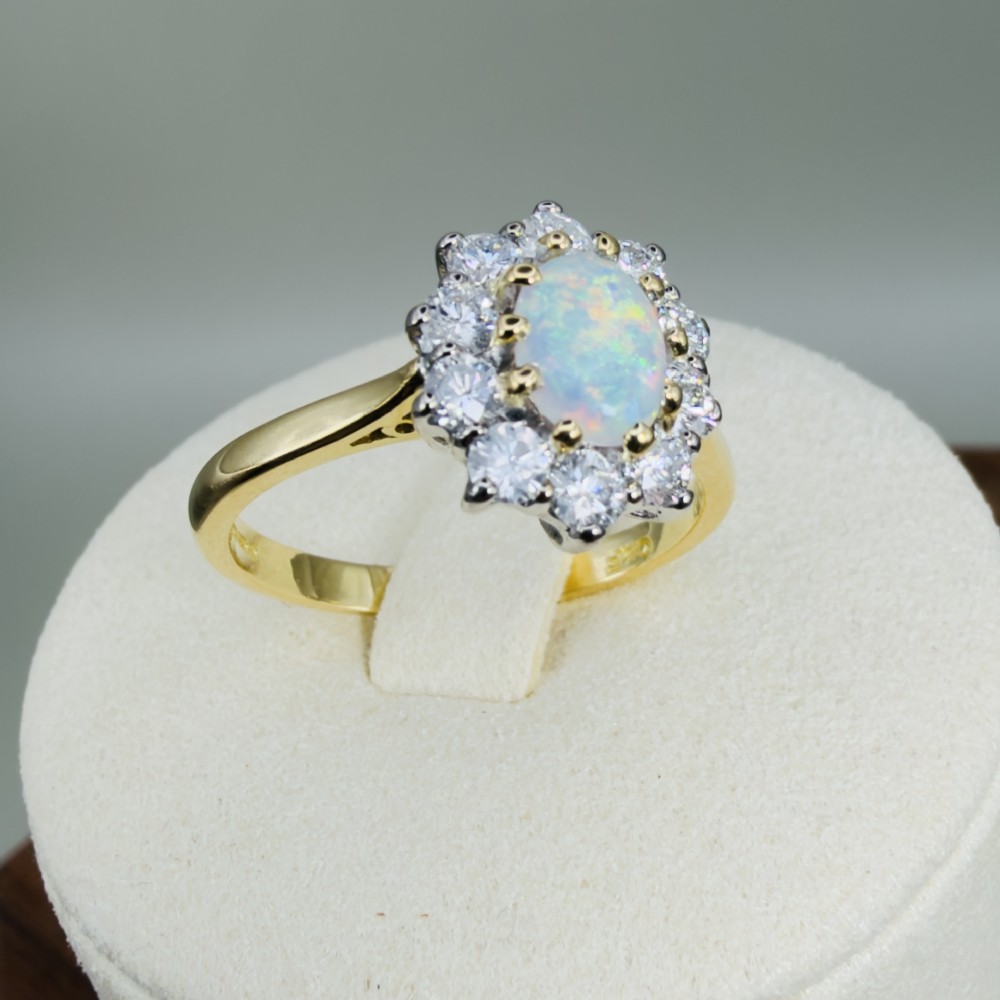 An 18ct yellow gold ring featuring an oval cabochon opal surrounded by a halo of brilliant-cut diamonds. View X