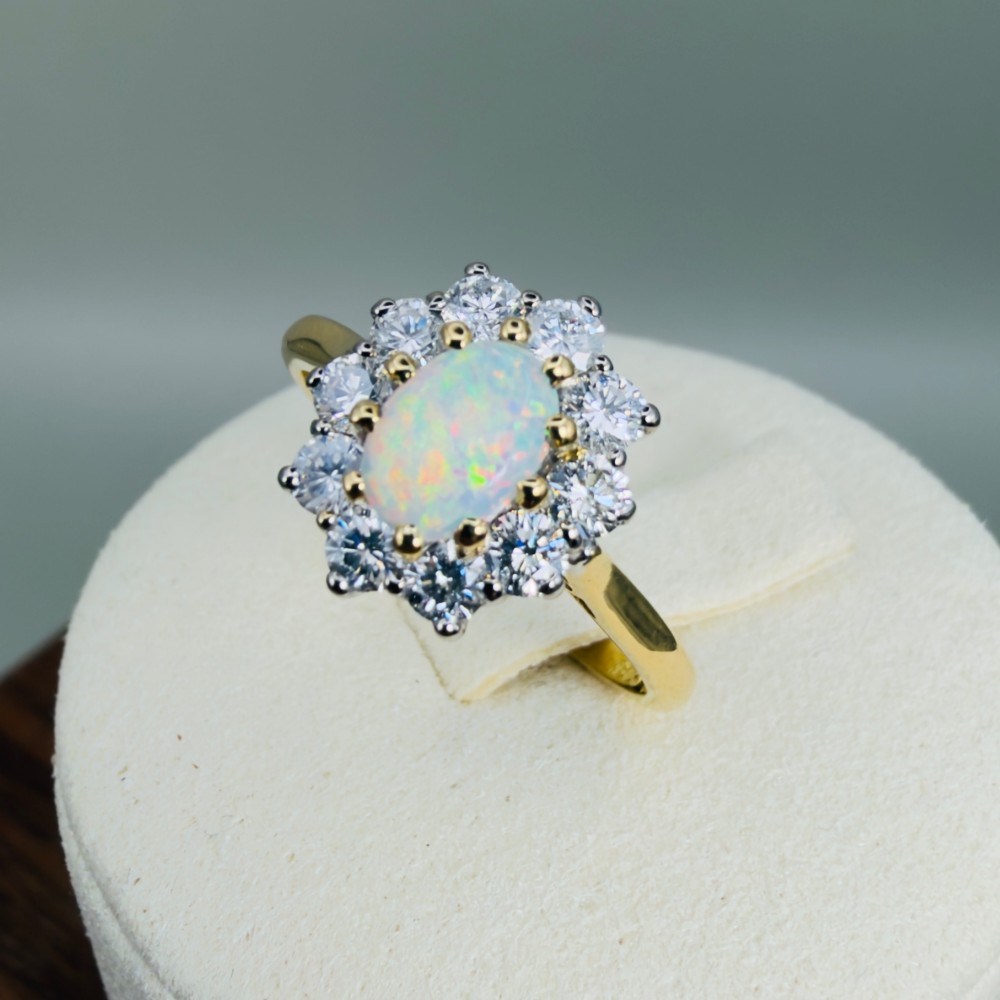 An 18ct yellow gold ring featuring an oval cabochon opal surrounded by a halo of brilliant-cut diamonds. View XI