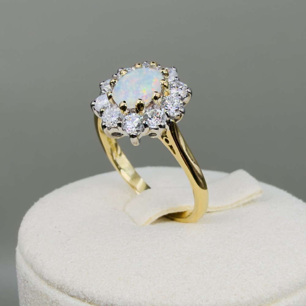 An 18ct yellow gold ring featuring an oval cabochon opal surrounded by a halo of brilliant-cut diamonds. View XII