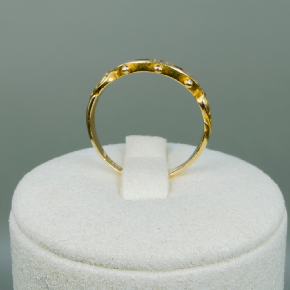 An 18ct yellow gold Edwardian trilogy ring set with a central round diamond flanked by two oval red rubies, featuring scroll detailing on the shoulders. View X