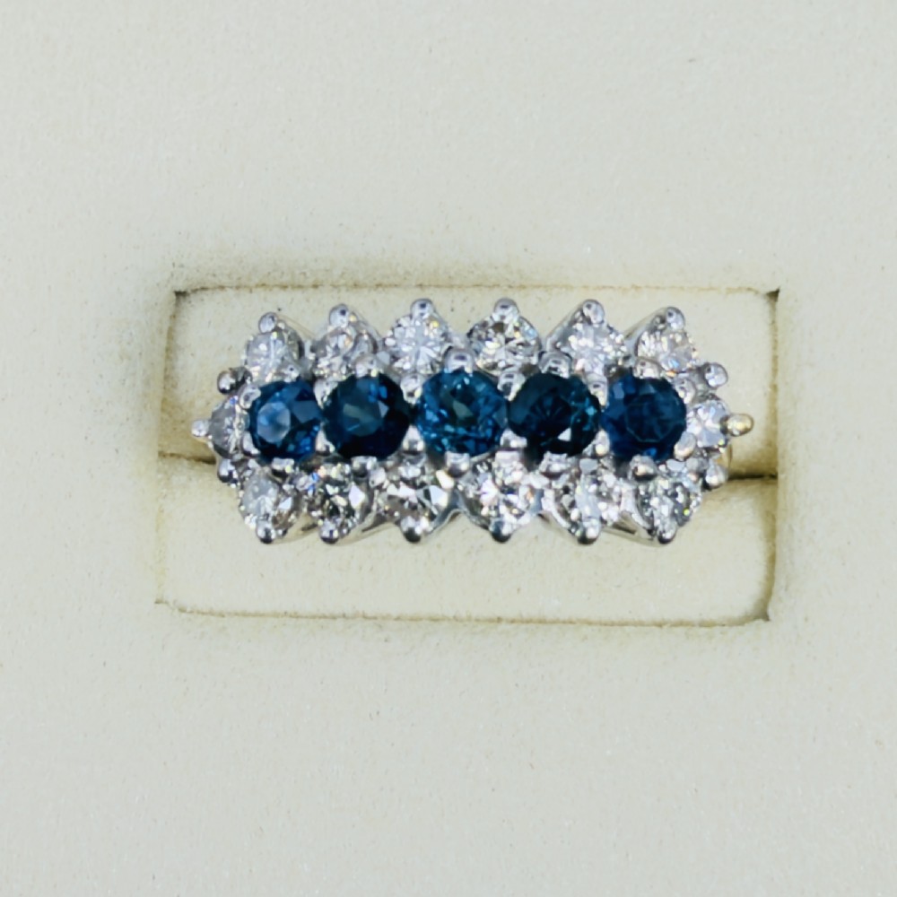 An 18ct gold cluster boat ring featuring five round blue sapphires surrounded by a halo of brilliant diamonds. View II