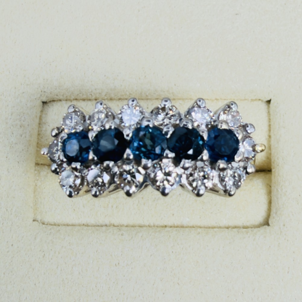 An 18ct gold cluster boat ring featuring five round blue sapphires surrounded by a halo of brilliant diamonds. View V