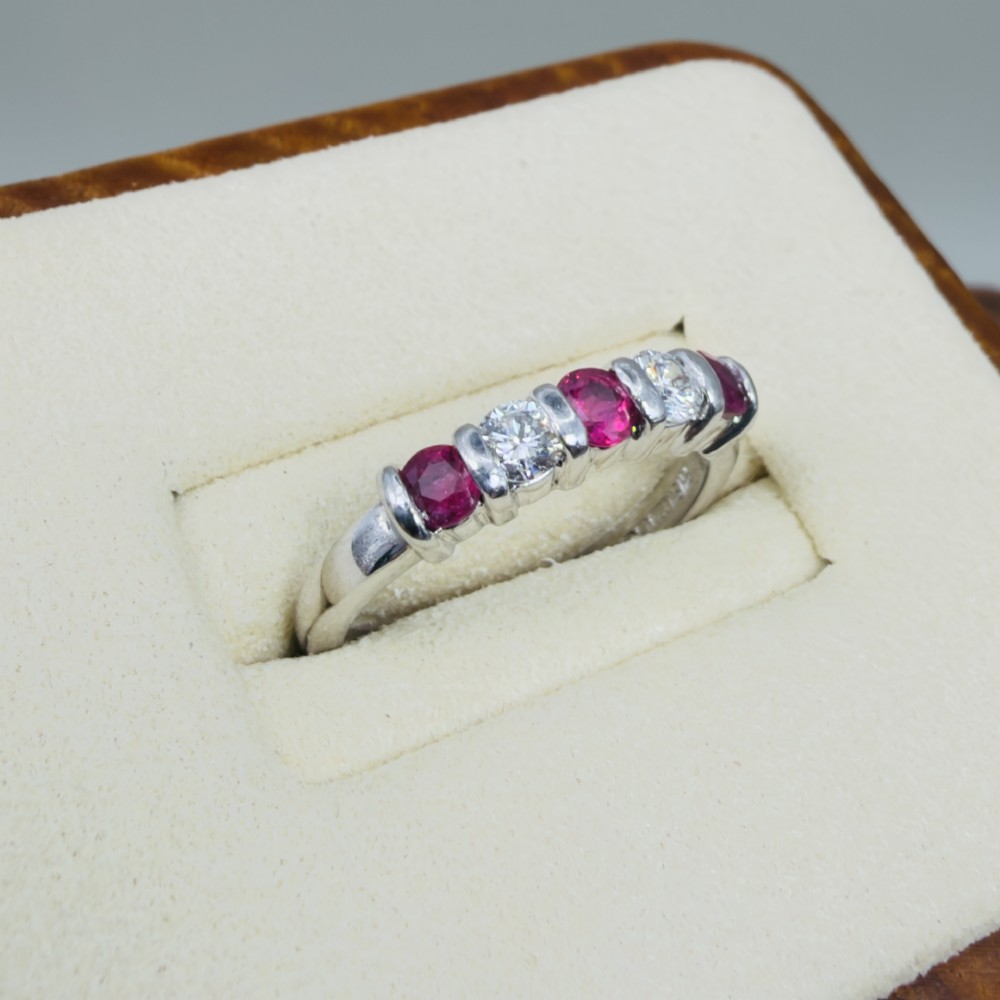An 18ct white gold band ring featuring three round red rubies alternating with two round diamonds in a bar setting. View IV