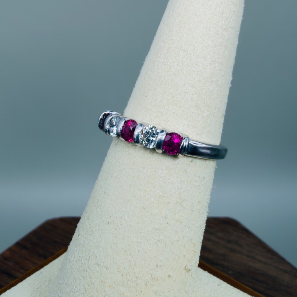 An 18ct white gold band ring featuring three round red rubies alternating with two round diamonds in a bar setting. View VI