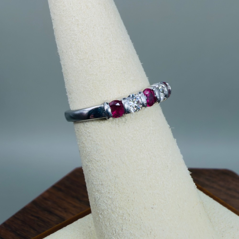 An 18ct white gold band ring featuring three round red rubies alternating with two round diamonds in a bar setting. View VII