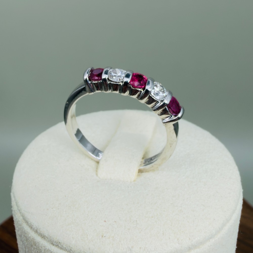 An 18ct white gold band ring featuring three round red rubies alternating with two round diamonds in a bar setting. View VIII