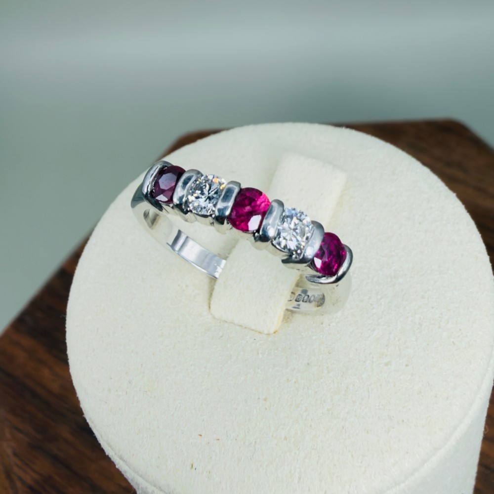An 18ct white gold band ring featuring three round red rubies alternating with two round diamonds in a bar setting. View IX