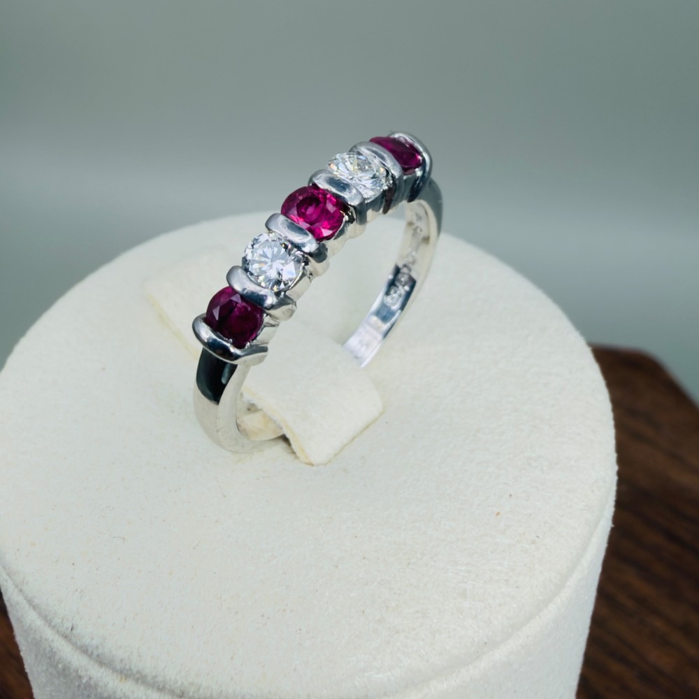 An 18ct white gold band ring featuring three round red rubies alternating with two round diamonds in a bar setting.