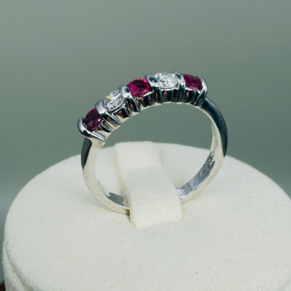 An 18ct white gold band ring featuring three round red rubies alternating with two round diamonds in a bar setting. View X