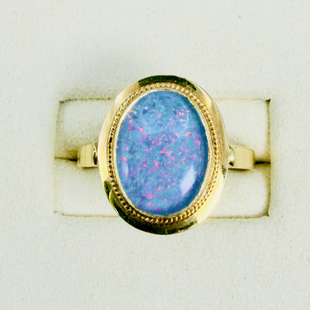 An oval blue boulder opal cabochon gemstone set in a 14ct yellow gold ring with a rope twist bezel border. View II