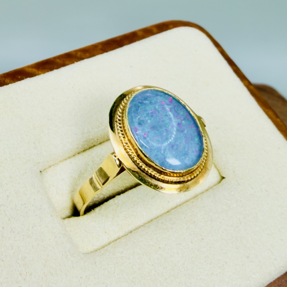 An oval blue boulder opal cabochon gemstone set in a 14ct yellow gold ring with a rope twist bezel border. View IV