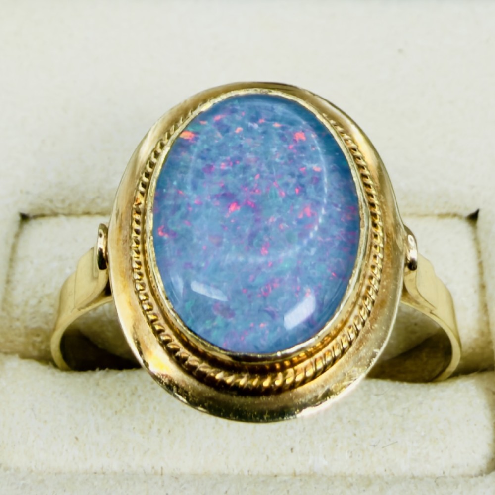 An oval blue boulder opal cabochon gemstone set in a 14ct yellow gold ring with a rope twist bezel border. View V