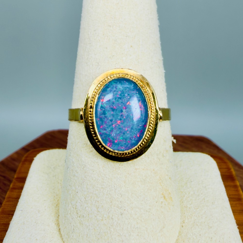 An oval blue boulder opal cabochon gemstone set in a 14ct yellow gold ring with a rope twist bezel border. View VI