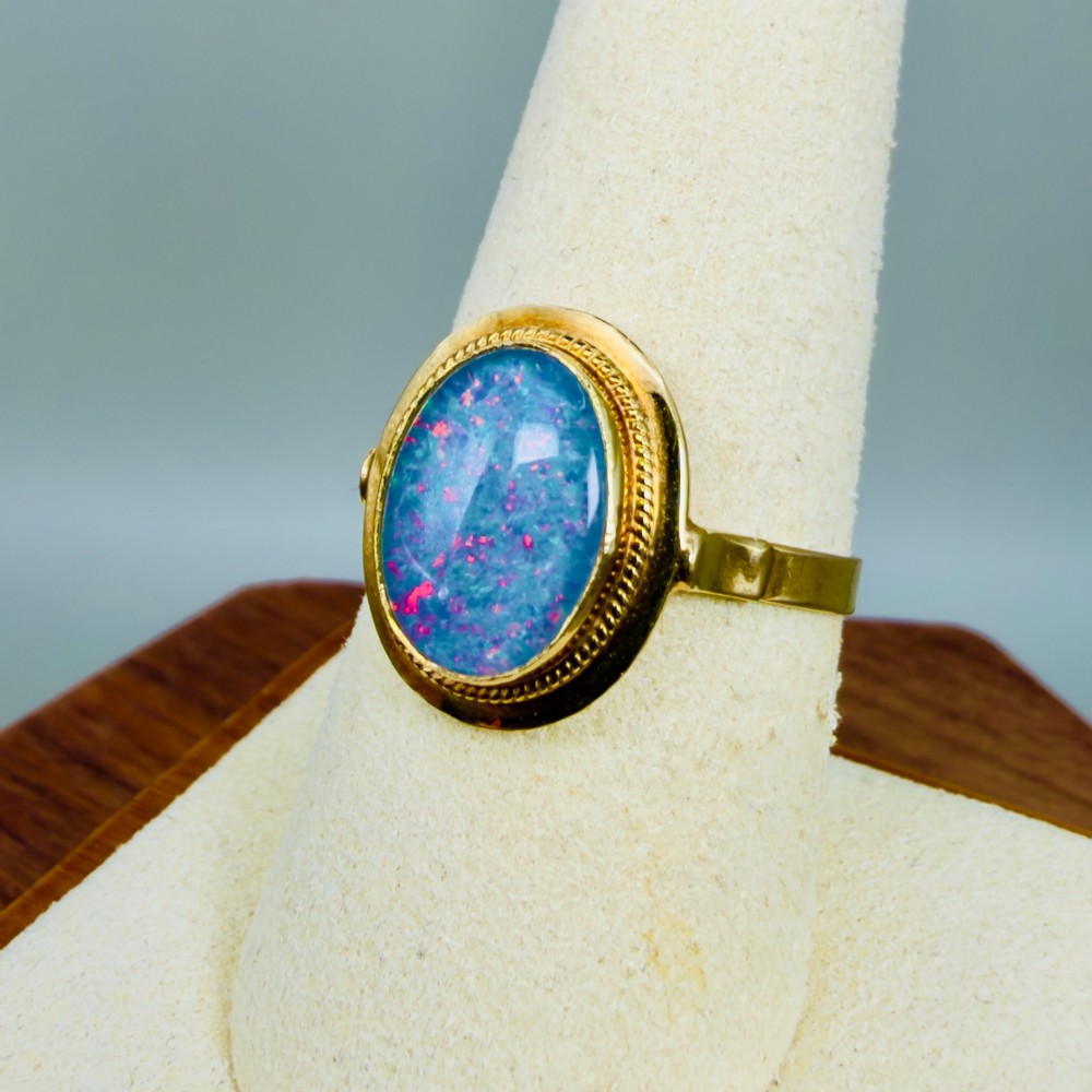 An oval blue boulder opal cabochon gemstone set in a 14ct yellow gold ring with a rope twist bezel border. View VII