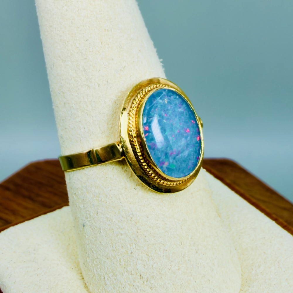 An oval blue boulder opal cabochon gemstone set in a 14ct yellow gold ring with a rope twist bezel border. View VIII