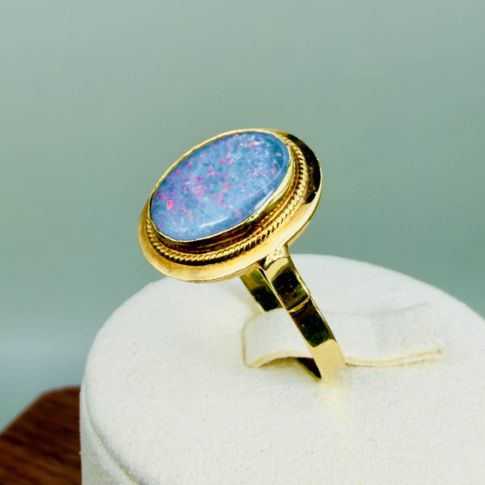 An oval blue boulder opal cabochon gemstone set in a 14ct yellow gold ring with a rope twist bezel border. View X