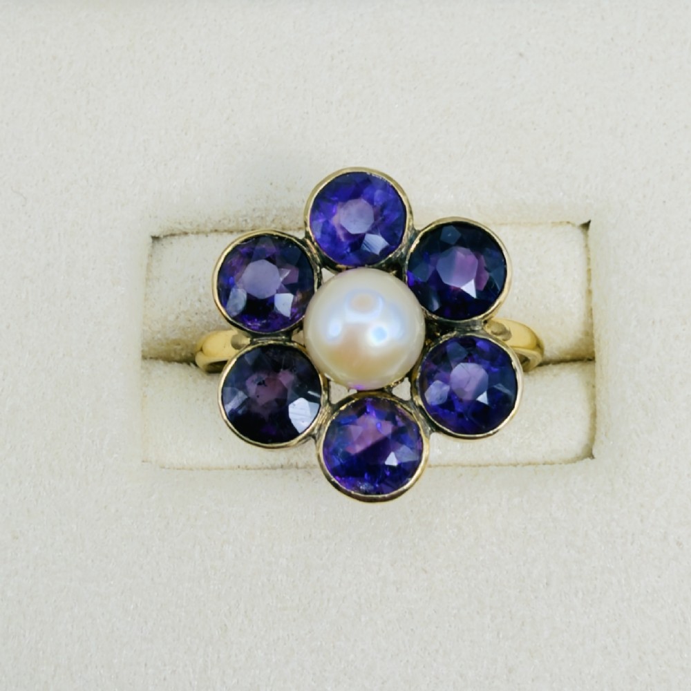 An 18ct gold Georgian cluster ring featuring a central round pearl encircled by six faceted purple amethysts in a floral arrangement. View II