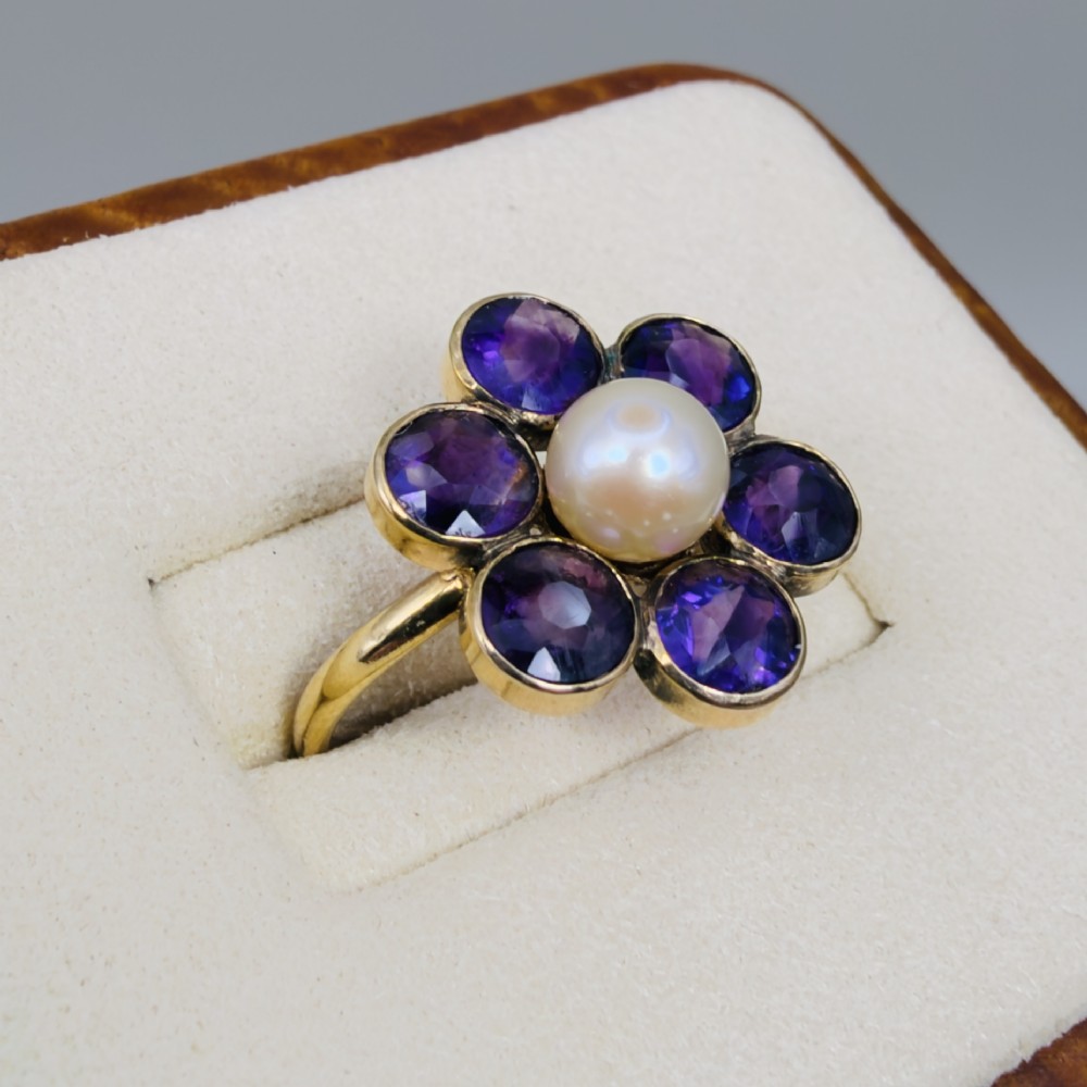 An 18ct gold Georgian cluster ring featuring a central round pearl encircled by six faceted purple amethysts in a floral arrangement. View IV