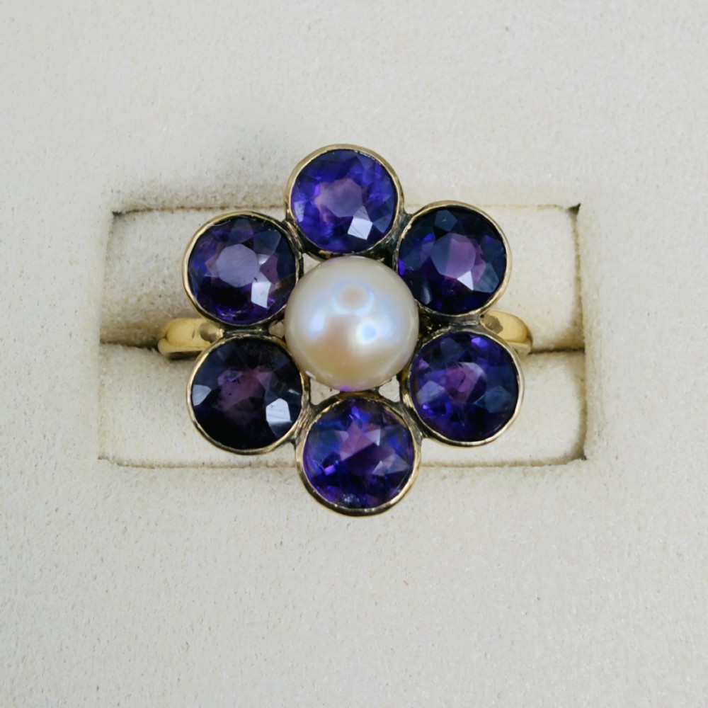 An 18ct gold Georgian cluster ring featuring a central round pearl encircled by six faceted purple amethysts in a floral arrangement. View V