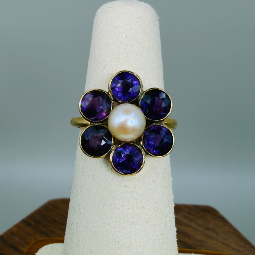 An 18ct gold Georgian cluster ring featuring a central round pearl encircled by six faceted purple amethysts in a floral arrangement. View VI
