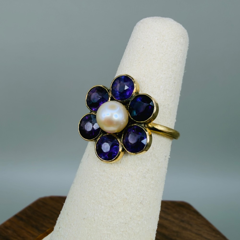 An 18ct gold Georgian cluster ring featuring a central round pearl encircled by six faceted purple amethysts in a floral arrangement. View VII