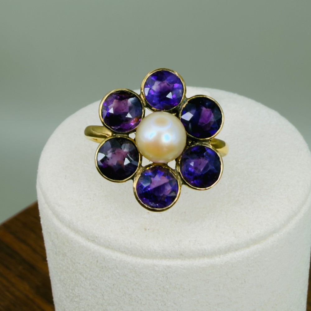 An 18ct gold Georgian cluster ring featuring a central round pearl encircled by six faceted purple amethysts in a floral arrangement. View IX