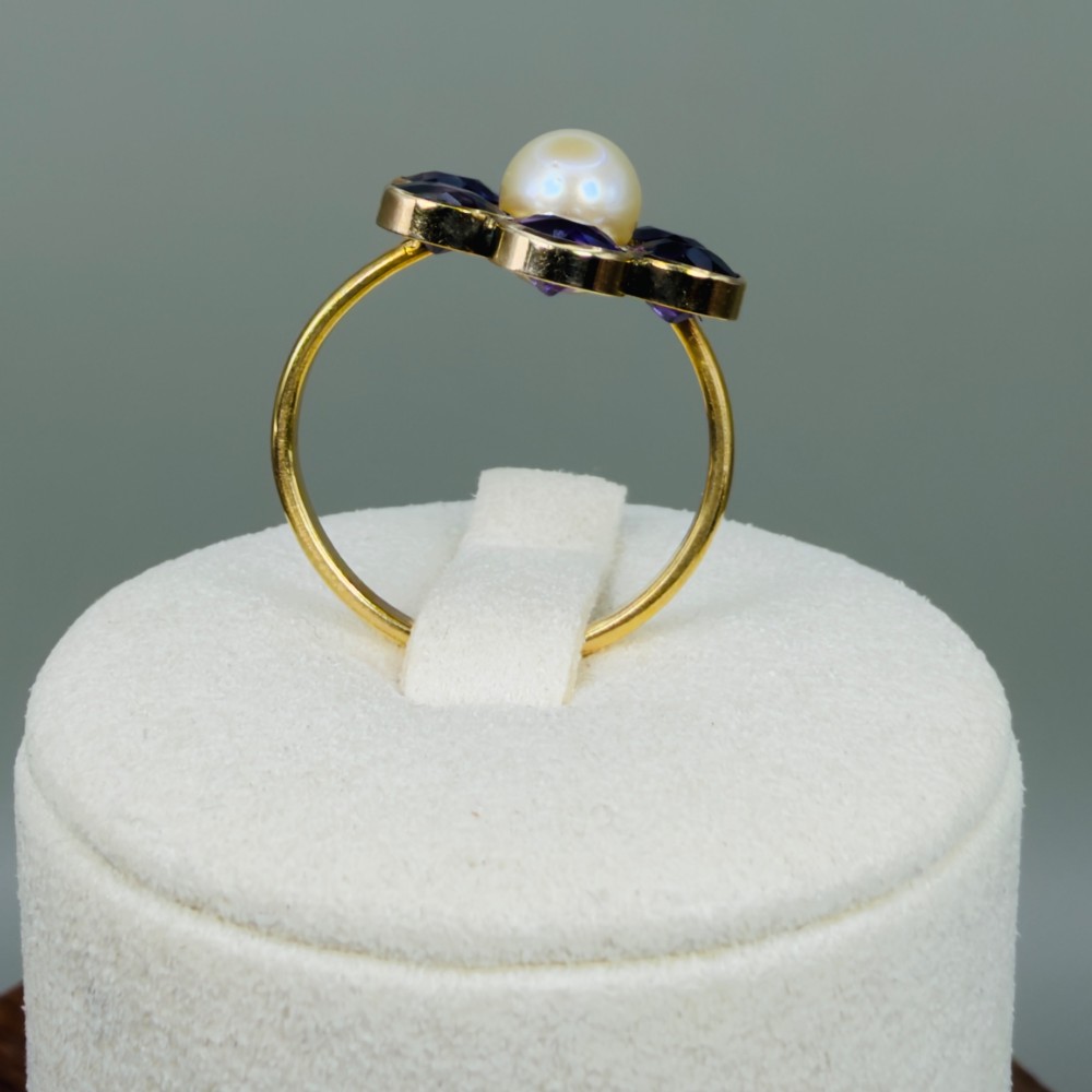 An 18ct gold Georgian cluster ring featuring a central round pearl encircled by six faceted purple amethysts in a floral arrangement. View X