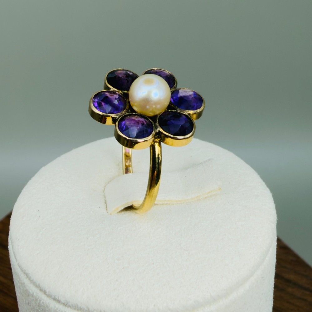 An 18ct gold Georgian cluster ring featuring a central round pearl encircled by six faceted purple amethysts in a floral arrangement. View XI