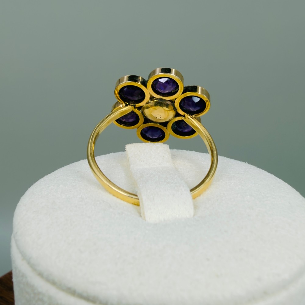 An 18ct gold Georgian cluster ring featuring a central round pearl encircled by six faceted purple amethysts in a floral arrangement. View XII