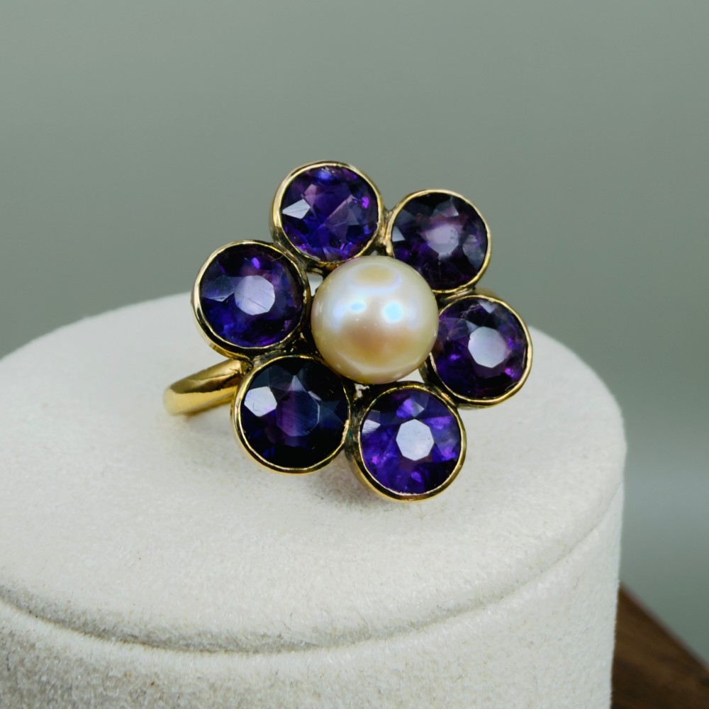 An 18ct gold Georgian cluster ring featuring a central round pearl encircled by six faceted purple amethysts in a floral arrangement.