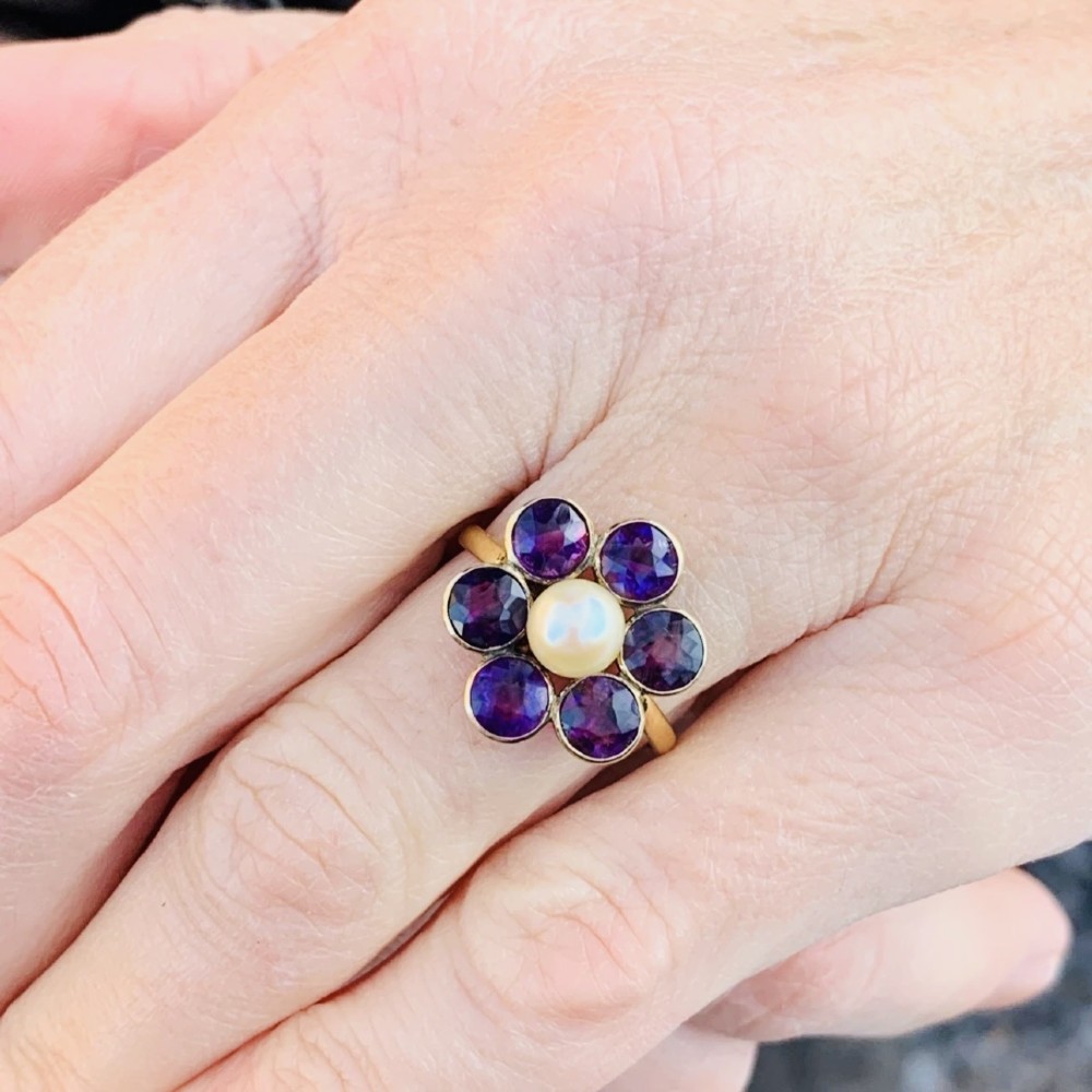 An 18ct gold Georgian cluster ring featuring a central round pearl encircled by six faceted purple amethysts in a floral arrangement. View XIII