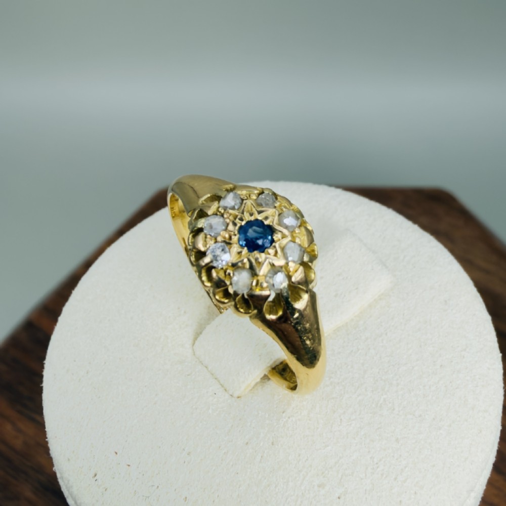 A mid-Victorian 18ct yellow gold ring featuring a central blue sapphire surrounded by a cluster of diamonds in a carved starburst setting.