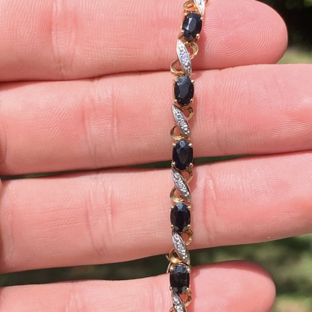 A 9ct yellow gold link bracelet set with oval-cut dark blue sapphires and accent diamond links, worn on a wrist. View II