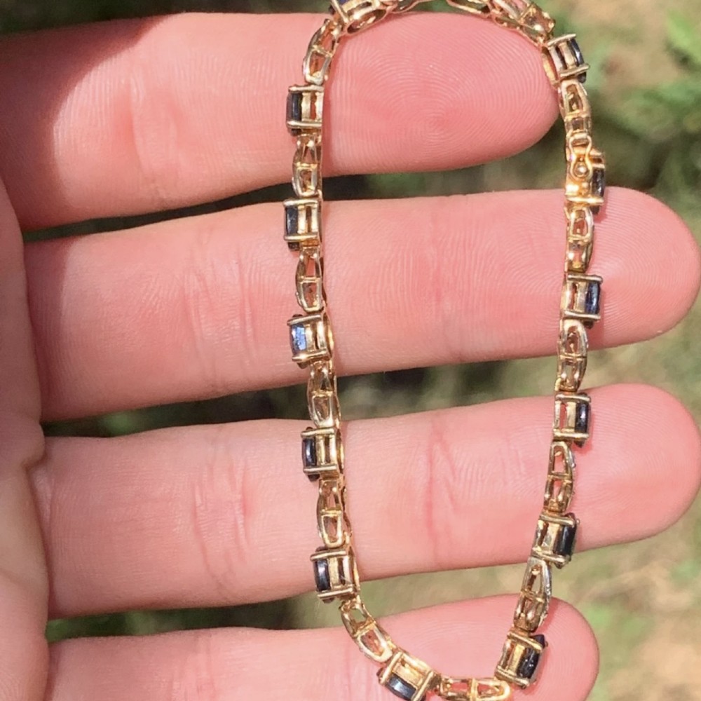 A 9ct yellow gold link bracelet set with oval-cut dark blue sapphires and accent diamond links, worn on a wrist. View VI