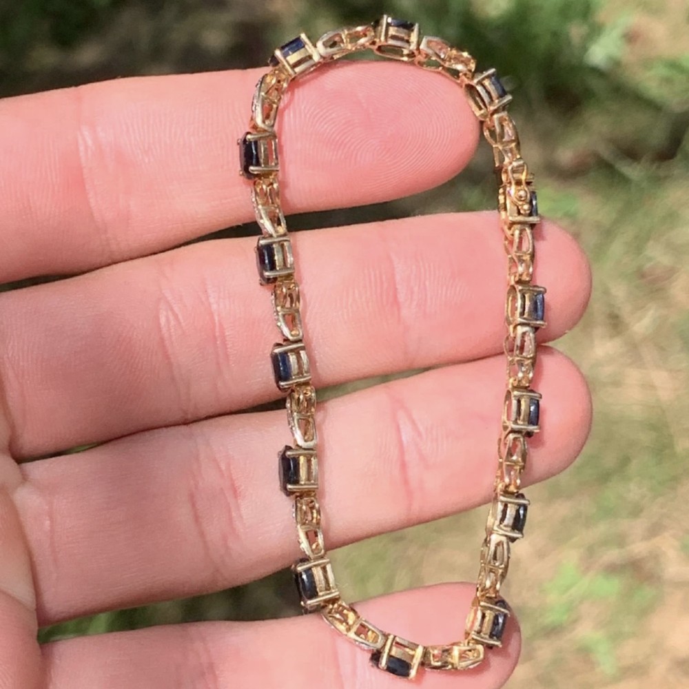A 9ct yellow gold link bracelet set with oval-cut dark blue sapphires and accent diamond links, worn on a wrist. View VII